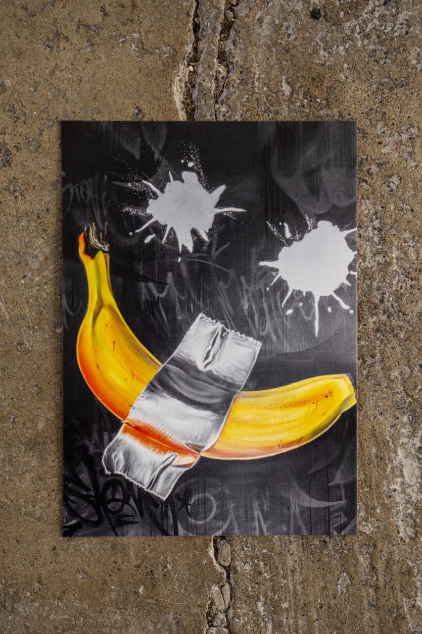 Diese Postkarte ist ein frecher Seitenhieb auf die Kunstwelt: Eine Banane, mit silbernem Tape an die Wand geklebt – inspiriert von einem berühmten Kunstwerk, aber mit urbanem Twist. Die Graffiti-Ästhetik, der dunkle Hintergrund und die weißen Farbspritzer verleihen dem Motiv eine rebellische Attitüde. Ironisch. Provokant. Und 100 % Street-Art.