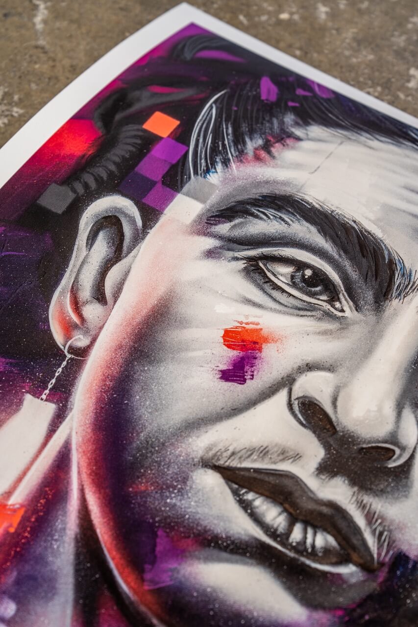 Detailaufnahme eines hochwertigen Graffiti-Art-Prints von Stone Graffiti. Das Motiv zeigt ein hyperrealistisches Porträt mit intensiven Schattierungen in Schwarz-Weiß, ergänzt durch abstrakte, leuchtende Farbakzente in Lila, Rot und Orange. Die fein ausgearbeiteten Gesichtszüge und der moderne, urbane Stil verleihen dem Kunstwerk eine kraftvolle Ausdrucksstärke. Der Print liegt auf einer Betonoberfläche, was den Street-Art-Charakter zusätzlich betont.