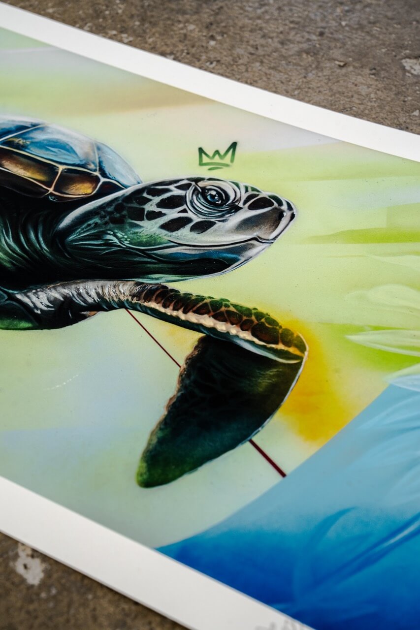 Detailaufnahme eines hochwertigen Kunstdrucks von Stone Graffiti. Die realistisch dargestellte Meeresschildkröte ist mit aufwendigen Schattierungen und Texturen versehen, die ihre Panzerstruktur und Hautdetails betonen. Über ihrem Kopf schwebt eine stilisierte Krone als künstlerisches Markenzeichen. Der Hintergrund zeigt weiche Farbverläufe in Gelb, Grün und Blau mit abstrakten Elementen. Die Komposition verbindet hyperrealistische Darstellung mit grafischen Akzenten und moderner Street-Art-Ästhetik.