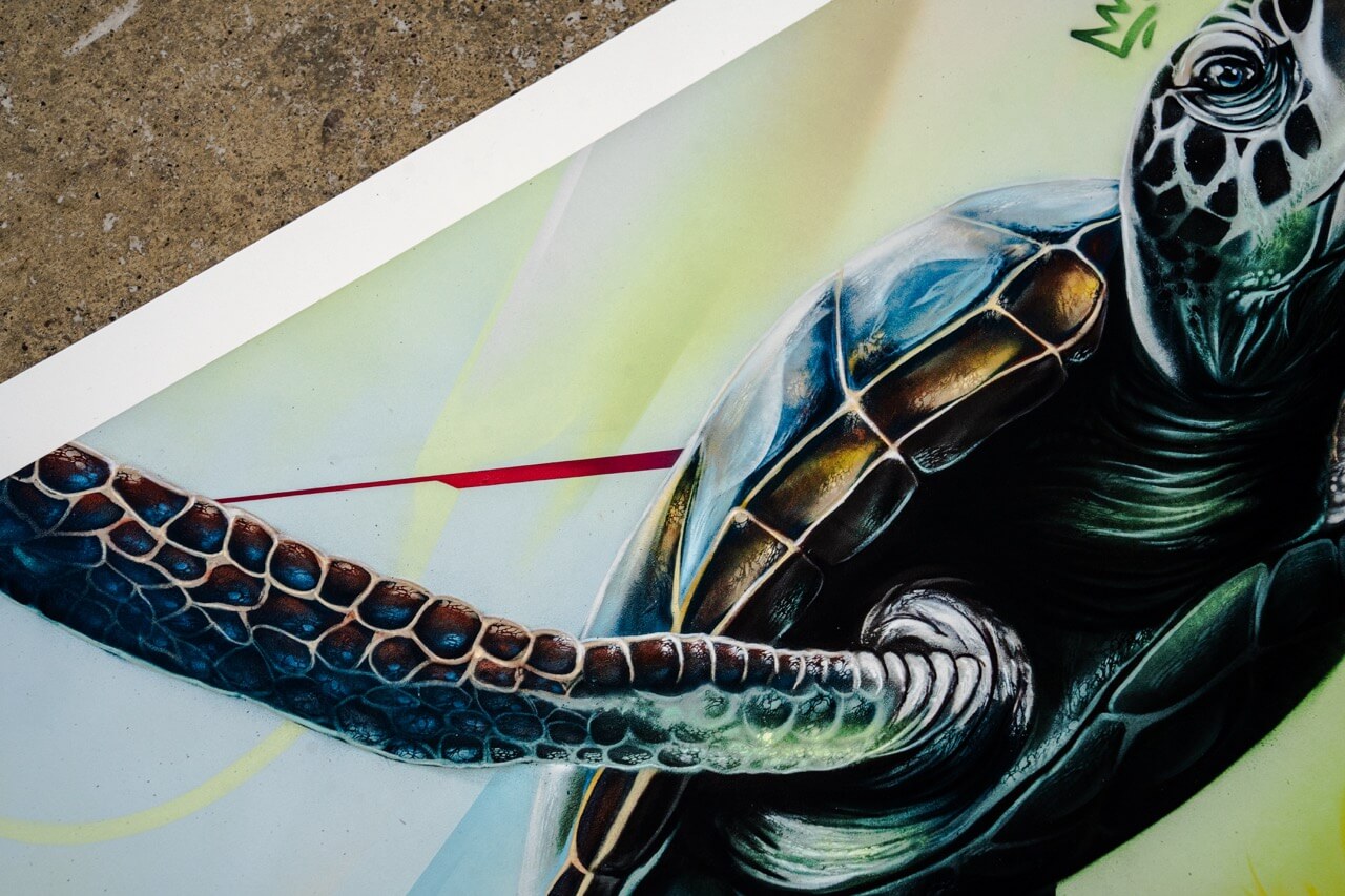 Detailaufnahme eines hochwertigen Kunstdrucks von Stone Graffiti. Die hyperrealistische Meeresschildkröte besticht durch detaillierte Texturen auf Panzer und Flossen. Der glänzende Panzer reflektiert Licht und erzeugt einen dreidimensionalen Effekt. Eine rote grafische Linie durchschneidet den sanften Farbverlauf im Hintergrund, der in Pastelltönen aus Gelb, Grün und Blau gehalten ist. Die stilisierte Krone über dem Kopf der Schildkröte dient als charakteristisches Markenzeichen.