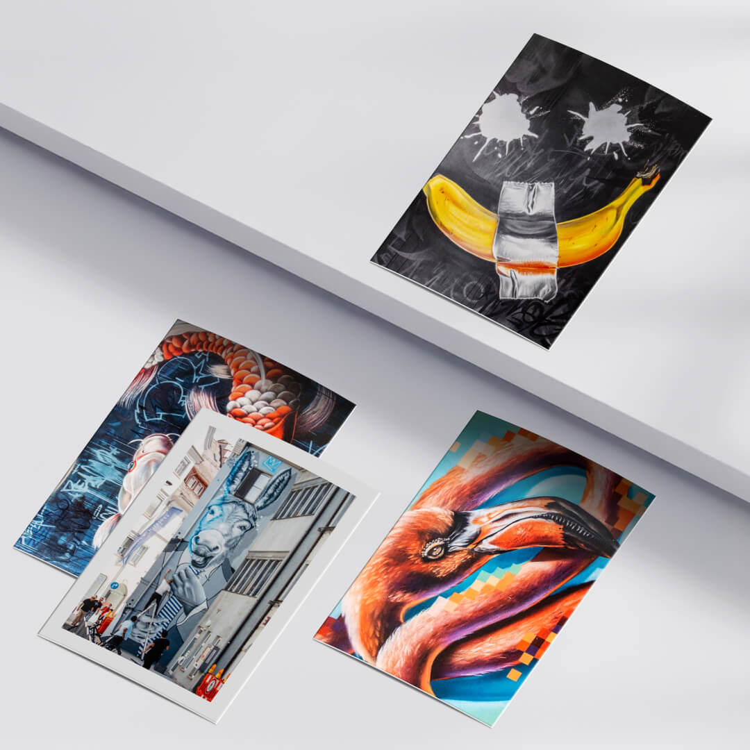 Vier Kunstpostkarten mit Graffiti-Motiven liegen auf einer weißen Oberfläche. Die Sammlung zeigt eine Mischung aus urbaner Street-Art und detailreichen Tierporträts mit kräftigen Farben und modernen Akzenten.