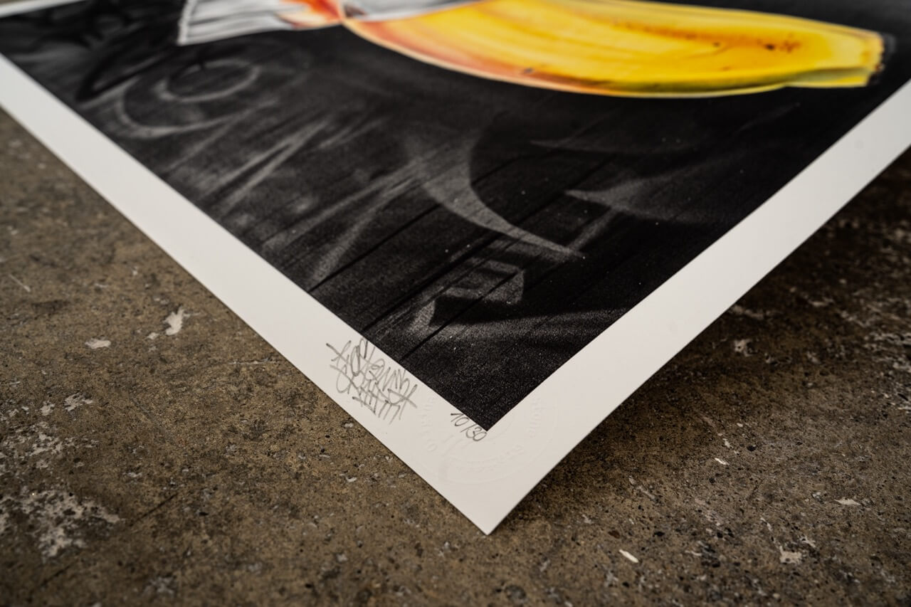 Der untere Rand eines hochwertigen Kunstdrucks zeigt die handschriftliche Signatur von Stone Graffiti und eine Prägung zur Echtheitszertifizierung. Das Motiv enthält eine gelbe Banane mit silbernem Klebeband auf dunklem Hintergrund.