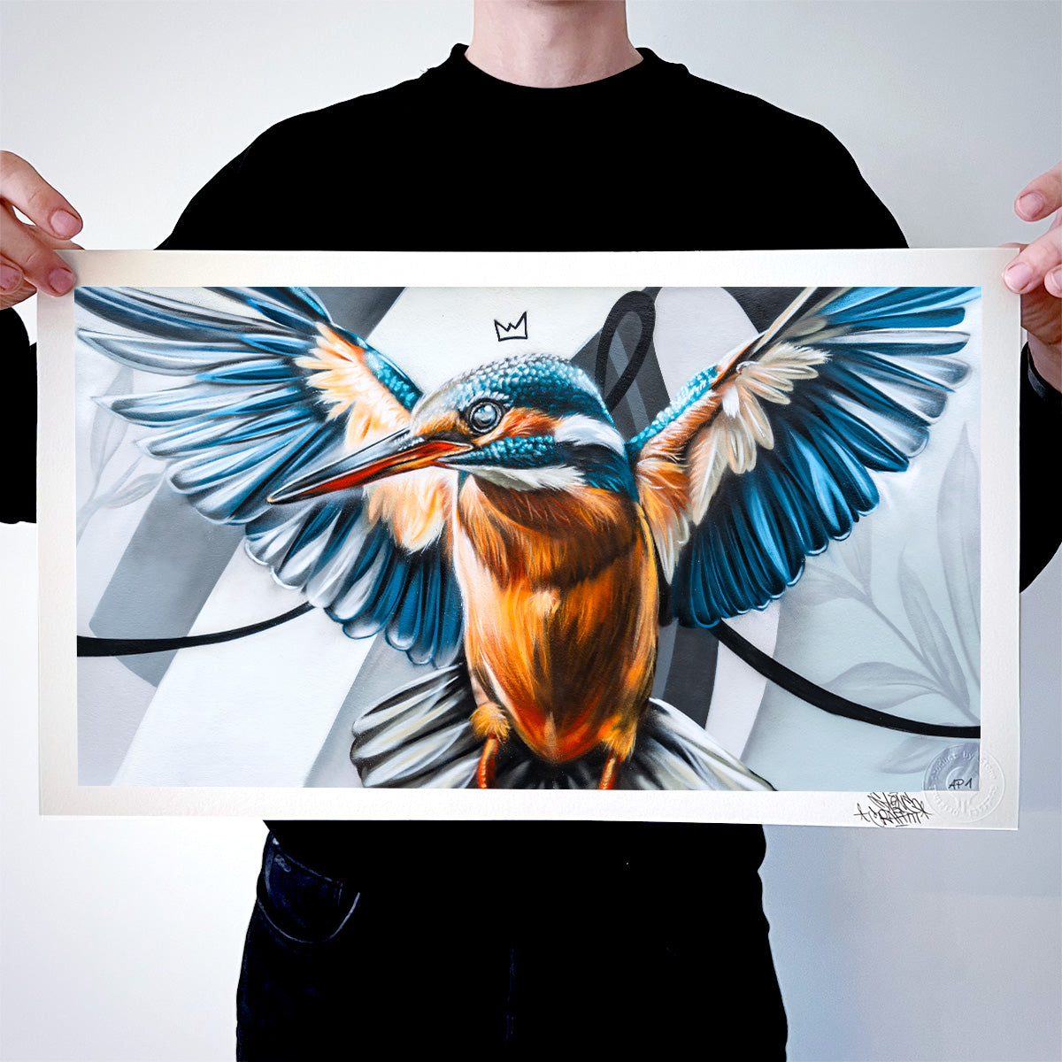 Das Bild zeigt eine Person, die einen Fine-Art-Print mit einem Eisvogel in leuchtenden Blau- und Orangetönen präsentiert. Das Motiv kombiniert fotorealistische Malerei mit urbanen, grafischen Elementen und verleiht dem Vogel eine majestätische Präsenz.