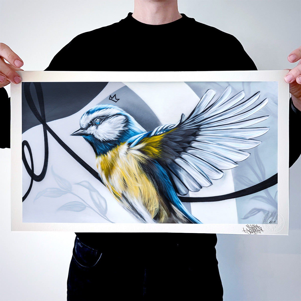 Das Bild zeigt eine Person, die einen hochwertigen Kunstdruck mit dem Motiv einer Blaumeise präsentiert. Die Vogelillustration ist in dynamischer Flugpose dargestellt und kombiniert realistische Details mit einem abstrakt-grafischen Hintergrund.