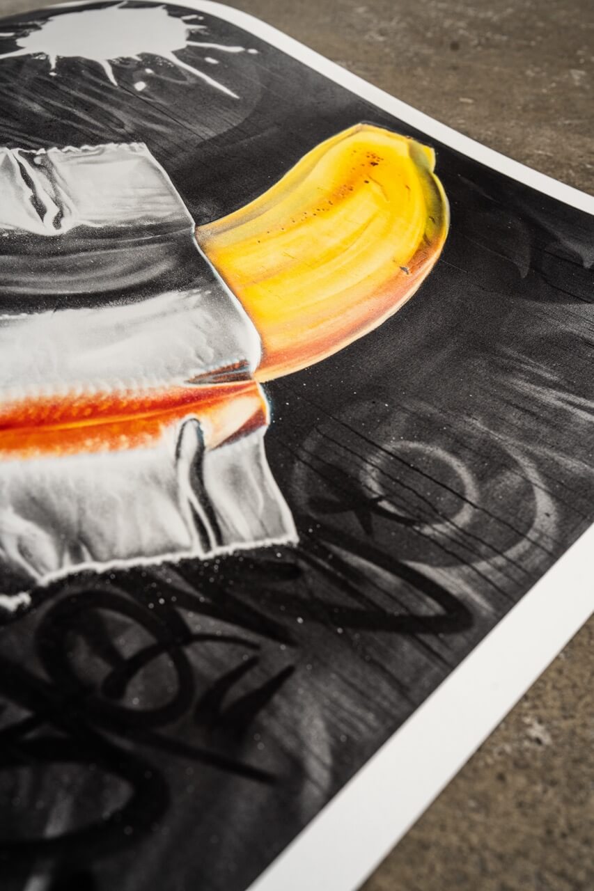 Detailaufnahme eines Graffiti-Kunstdrucks von Stone Graffiti. Das Motiv zeigt eine gelbe Banane, die mit silbernem Klebeband scheinbar auf einer dunklen Oberfläche befestigt ist. Der Hintergrund ist mit gesprühten Graffiti-Tags und subtilen Texturen gestaltet. Die kräftigen Farben der Banane setzen sich kontrastreich vom tiefschwarzen Untergrund ab und erzeugen eine moderne Street-Art-Ästhetik.