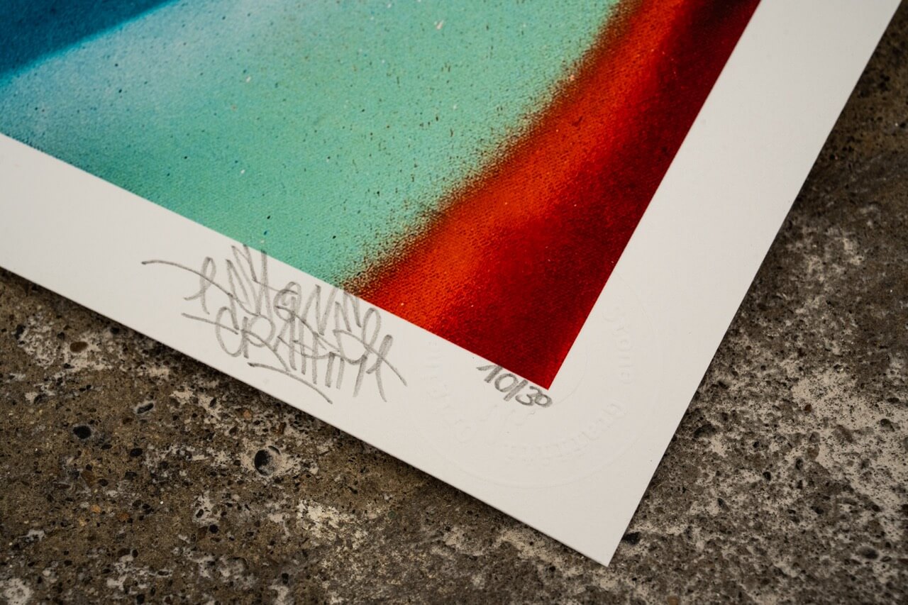 Detailaufnahme der unteren Ecke eines hochwertigen Graffiti-Kunstdrucks von Stone Graffiti. Der Print zeigt eine farbintensive Mischung aus Türkis und Rot mit weichen Farbübergängen. Die handschriftliche Signatur des Künstlers ist auf dem weißen Rand sichtbar, ebenso wie eine Prägung als Echtheitszertifikat. Der Druck liegt auf einer rauen Betonoberfläche, was den urbanen Charakter des Kunstwerks betont.