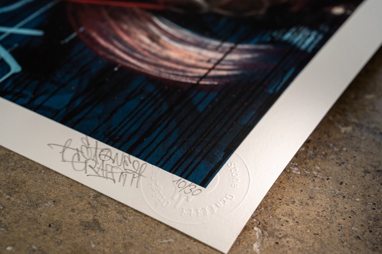 Detailaufnahme eines limitierten Kunstdrucks von Stone Graffiti, nummeriert als 10/30. Die Signatur des Künstlers ist mit Bleistift auf der unteren linken Ecke des Drucks angebracht. Neben der Signatur ist das geprägte Echtheitssiegel sichtbar. Der Druck zeigt eine dunkle, intensive Farbpalette mit blauen und roten Farbtönen sowie abstrakten Tropfspuren, die dem Werk eine dynamische und raue Street-Art-Ästhetik verleihen.
