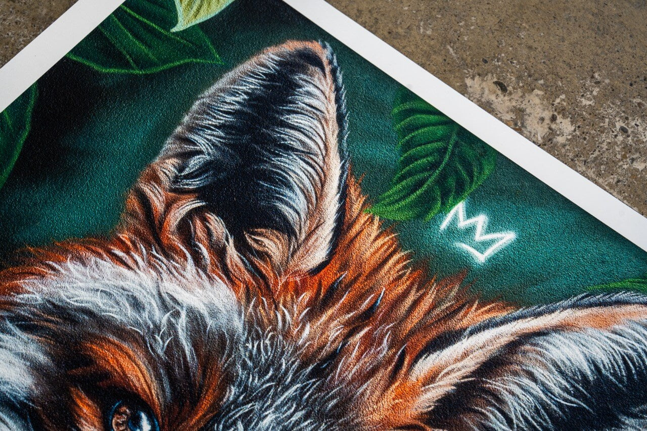 Nahaufnahme eines Kunstdrucks mit dem oberen Teil eines Fuchskopfes. Die detaillierte Fellstruktur in warmen Orange-, Weiß- und Schwarztönen hebt sich von einem satten grünen Hintergrund mit Blättern ab. Eine kleine, leuchtend weiße Krone schwebt über dem Kopf des Fuchses, was dem Bild eine majestätische Note verleiht. Die fein sichtbare Textur des Drucks verstärkt die Tiefe und Detailgenauigkeit des Motivs.
